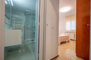 Ein Hotelzimmer mit einer Duschkabine aus Glas, einer weißen Tür und einer Holztür, die in einen anderen Raum führt.