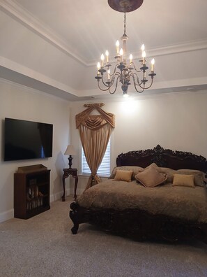 Une chambre à coucher avec un grand lit, un lustre, une télévision et une bibliothèque.