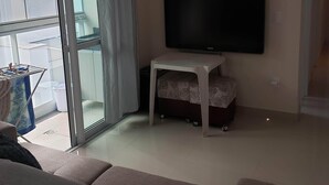 Una sala de estar con una televisión de pantalla plana sobre un mueble, un sofá, una puerta corrediza de vidrio y un equipo de aire acondicionado en la pared.