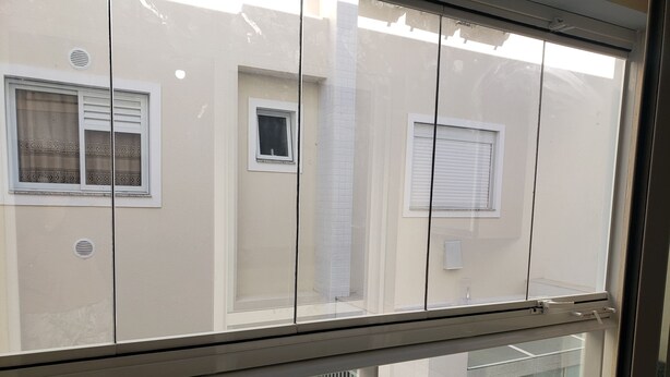 Vista a través de una ventana con barandilla metálica, que muestra un edificio con numerosas ventanas y un muro de azulejos.