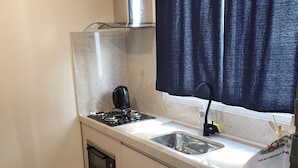 Una cocina compacta con estufa a gas, horno integrado, un lavamanos y una ventana con cortinas oscuras.