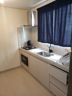 A compact kitchen with a gas stove, a built-in oven, a sink, and a window with dark curtains. - Apartment on Palmas beach (Governador Celso Ramos)