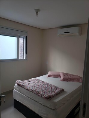 Quarto com cama, janela e ar condicionado.