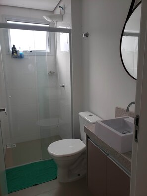 Uma casa de banho moderna com chuveiro envolto em vidro, sanita branca e lavatório com bancada de granito.