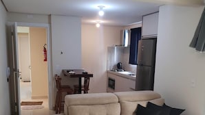 Sala de estar con sofá color beige, una mesa de comedor y una zona de cocina con refrigerador y estufa.