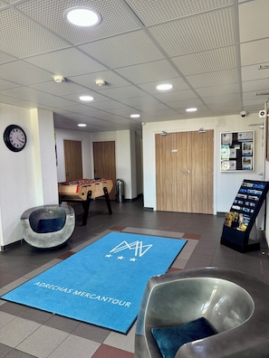 A lobby with a foosball table, a blue mat with 'ADRECHAS MERCANTOUR' text, a round seating area, and a door with a sign. - ADRECHAS MERCANTOUR (Valdeblore)