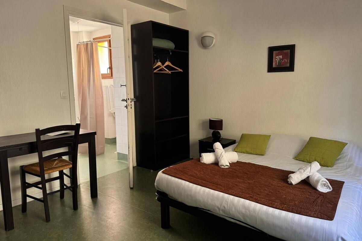 A bedroom with a bed, a desk, a chair, a wardrobe, and a nightstand.