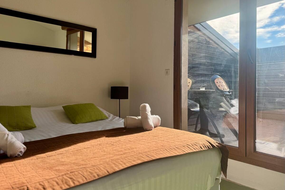 A hotel room with a bed, a window, a mirror, and a view of the outside.