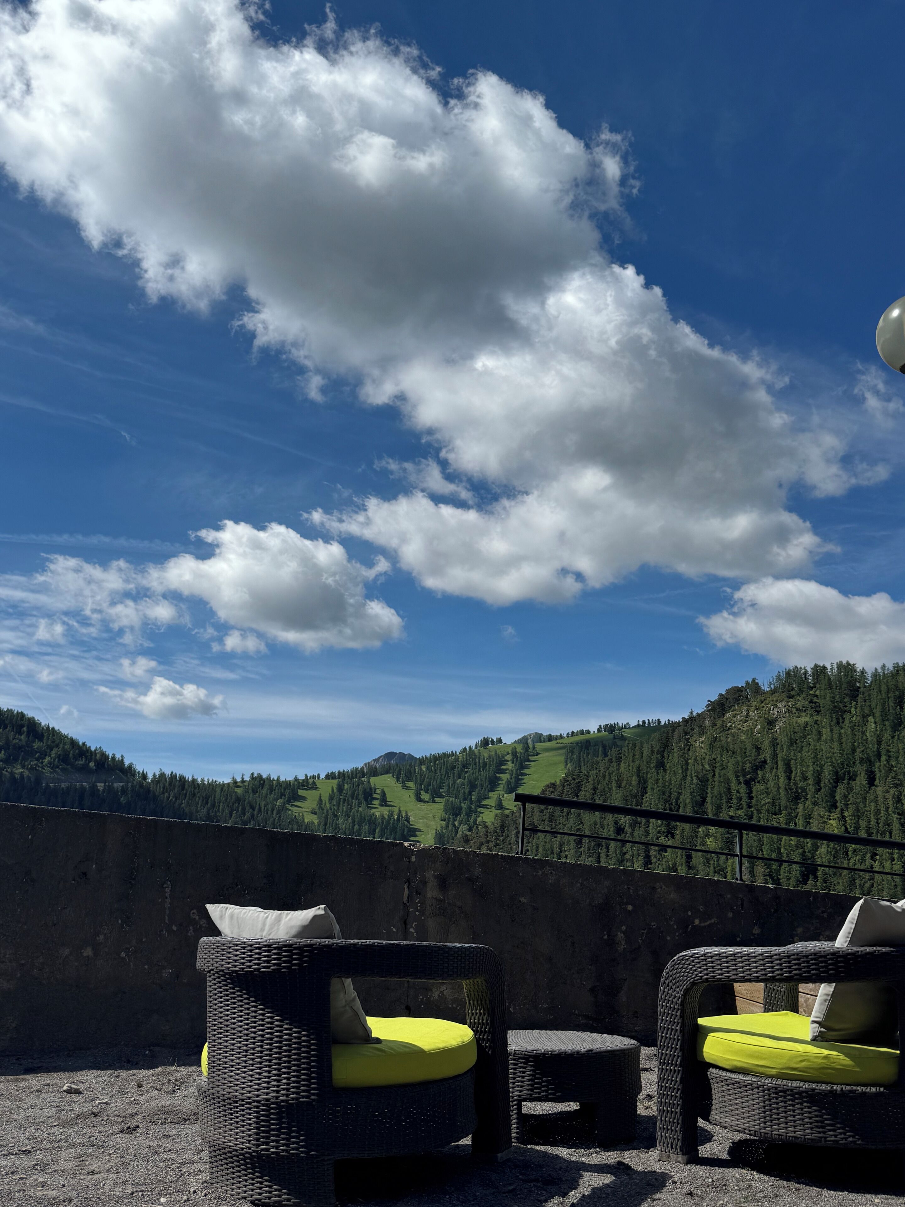 An outdoor seating area with wicker chairs and cushions, overlooking a mountainous landscape.