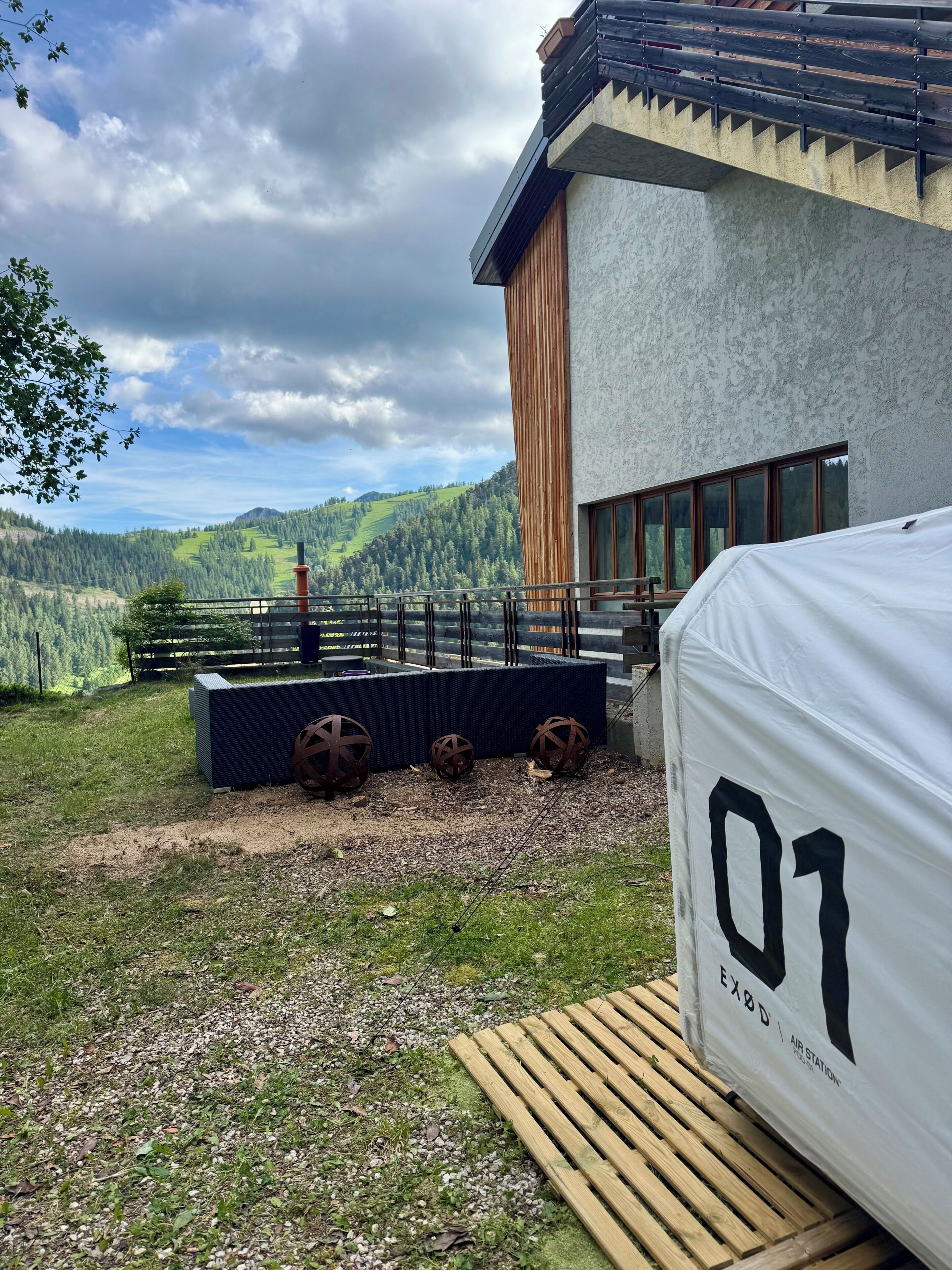 En moderne bygning med store vinduer, en balkon med gelænder og udsigt over en grøn dal.