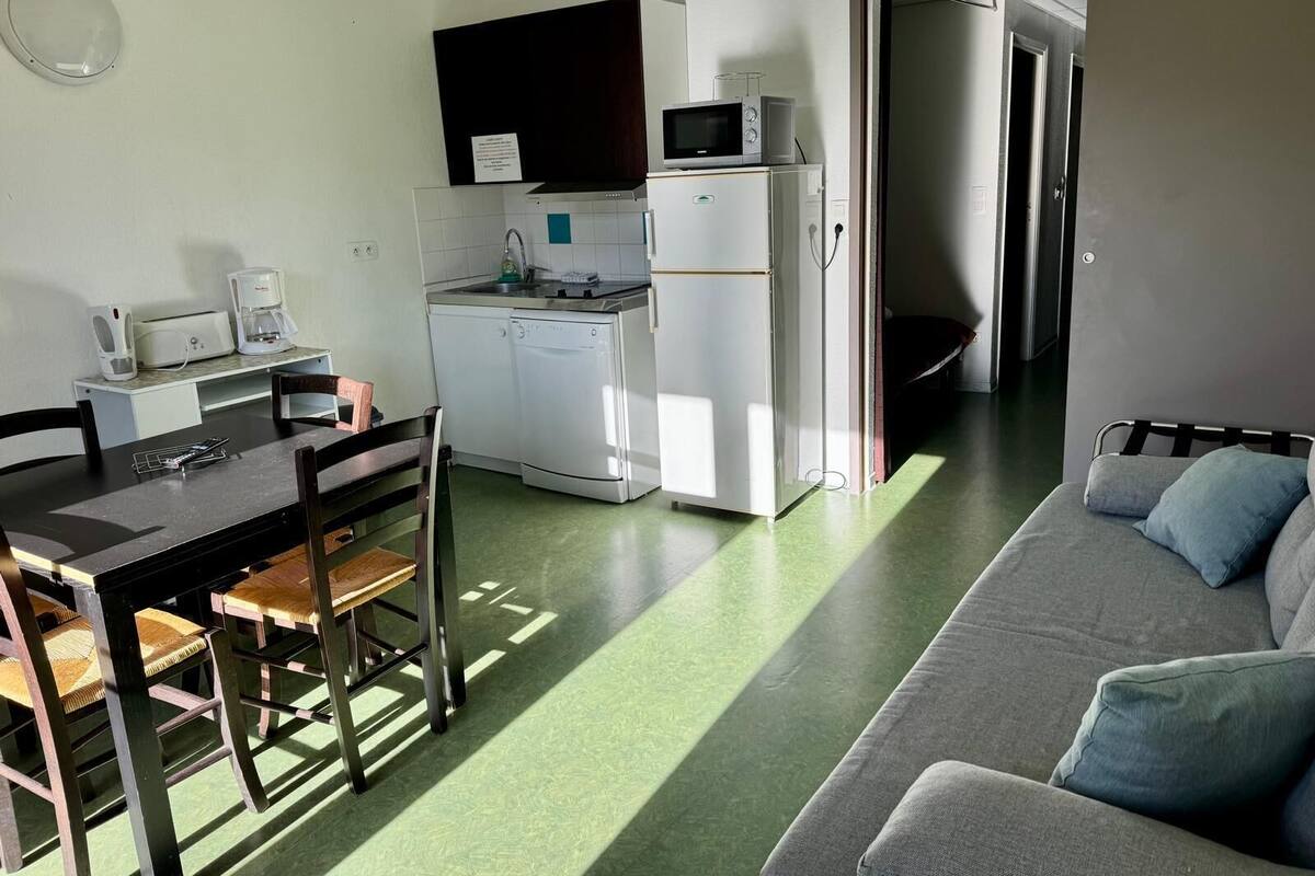 A compact kitchen with a microwave, coffee maker, and dishwasher. There is a dining table with chairs and a sofa in the living area.