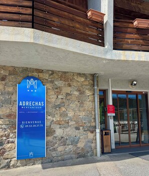 A stone wall with a blue signboard for Adrechas Mercantour, listing amenities like a hotel, restaurant, and spa. - ADRECHAS MERCANTOUR (Valdeblore)