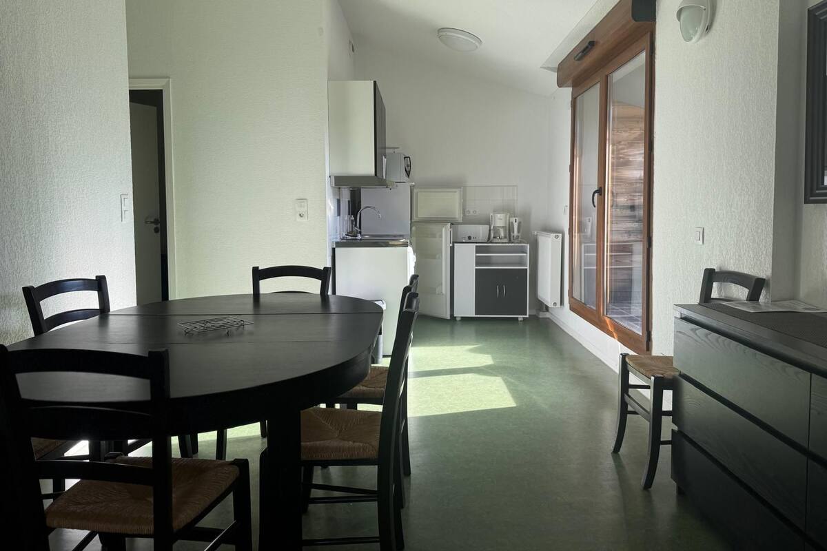 A compact kitchen with a dining table and chairs, a refrigerator, a coffee maker, and a window with a view.