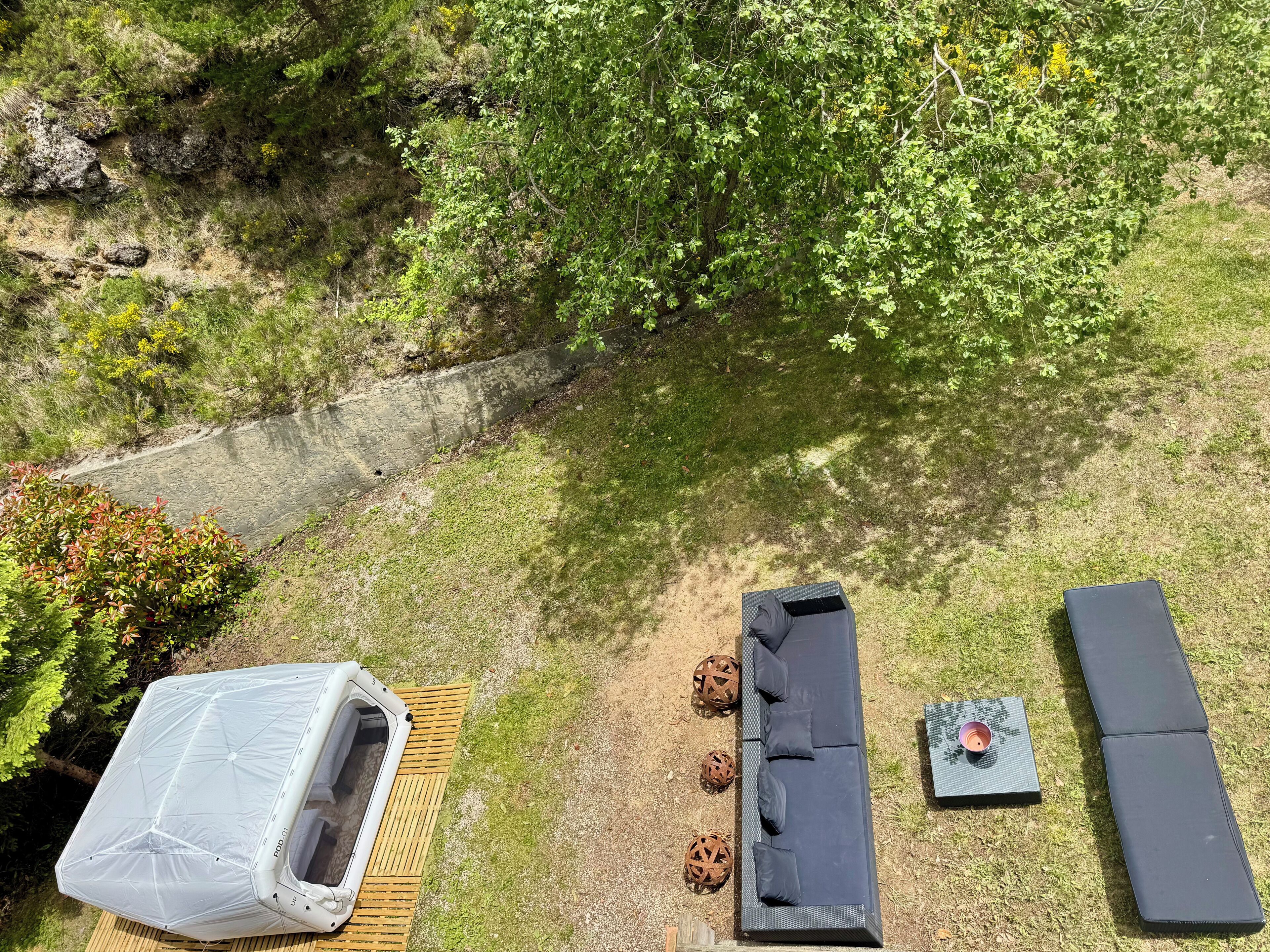 Un espace extérieur aménagé avec un canapé, des coussins, une table et une structure couverte.