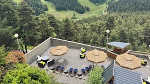 Une terrasse avec des sièges extérieurs, des parasols et une vue sur un paysage montagneux.
