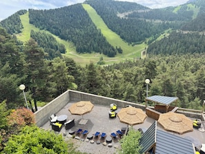 Una terrazza con posti a sedere all'aperto, ombrelloni e vista su un paesaggio montuoso.
