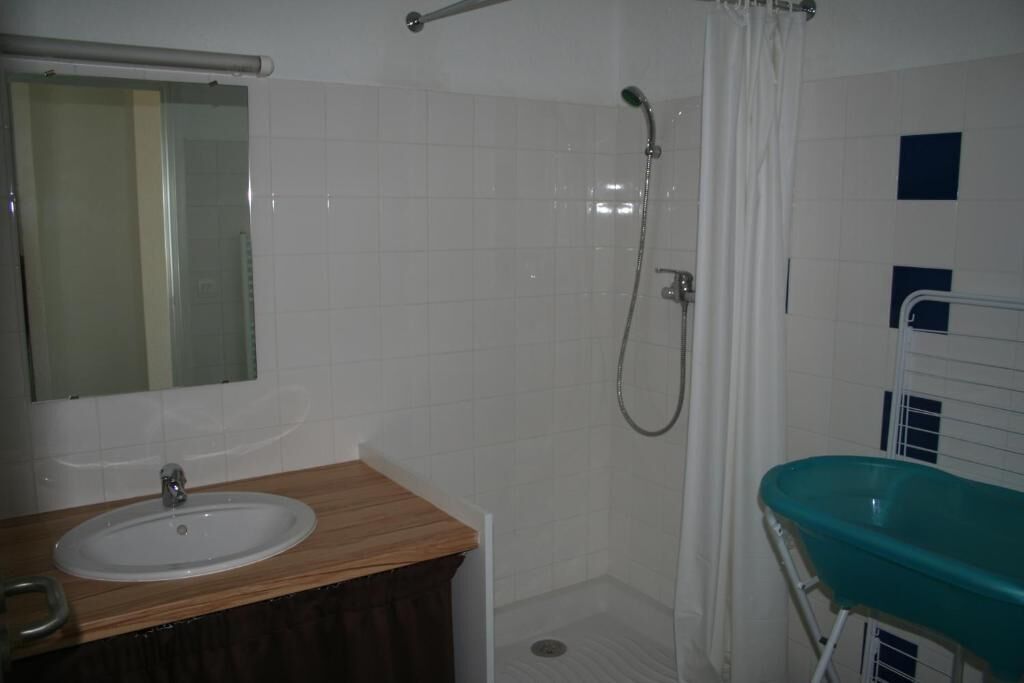 Une salle de bain avec un meuble-lavabo en bois, un évier, un miroir, une douche avec un rideau et une baignoire verte.