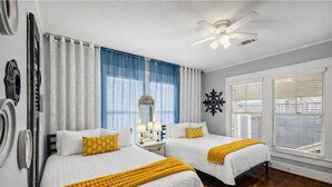 Ein Hotelzimmer mit zwei Betten, einem Deckenventilator, einem Fenster mit Jalousien und einer Wanddekoration.