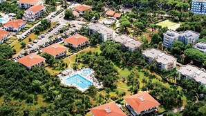 Ett flygbildsbild av ett bostadsområde med flera tvåvåningshus, en central pool och omgivande grönska.
