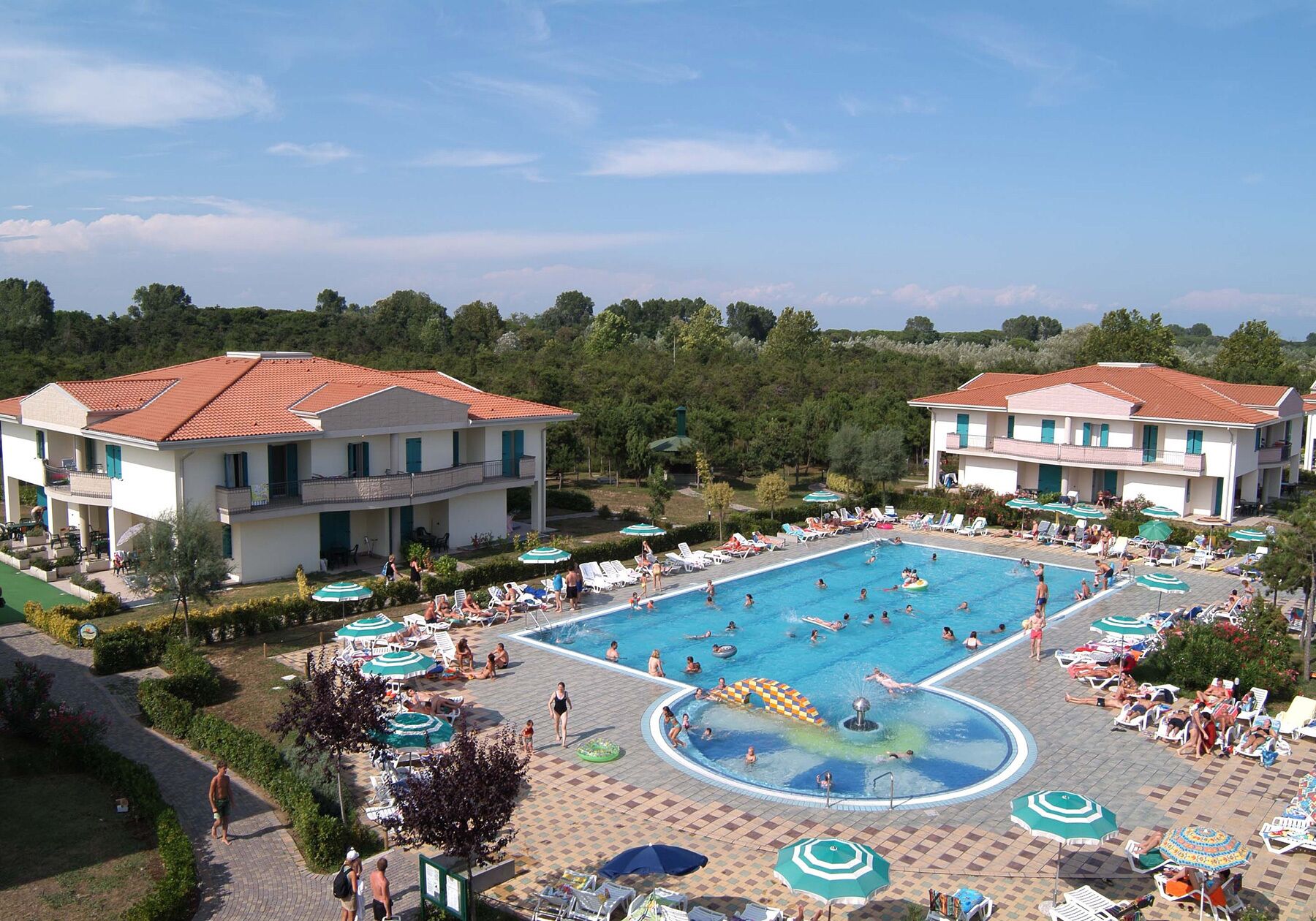 A large swimming pool surrounded by lounge chairs and umbrellas, with buildings in the background.