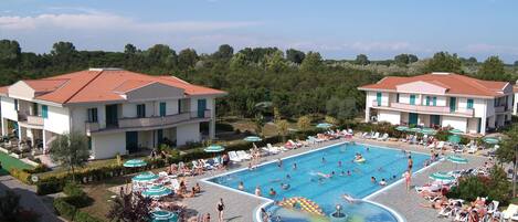 A large swimming pool surrounded by lounge chairs and umbrellas, with buildings in the background.