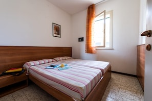 A bedroom with a wooden bed, a bedside table, a window with curtains, and a small framed picture on the wall. - Residence Michelangelo two-room apartment B4*+ facing the pool first floor for 4 persons (Bibione)