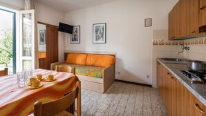 A compact room with a bed, a dining table, a kitchen area, and a window with curtains. - Residence Michelangelo two-room apartment B4*+ facing the pool first floor for 4 persons (Bibione)