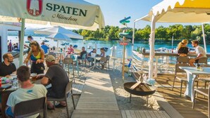 Un ristorante sul lungolago con posti a sedere all'aperto, un cartello con scritto 'SPATEN München' e vista sul lago.