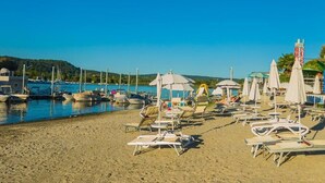 Una spiaggia con lettini e ombrelloni, barche ormeggiate in acqua e un cielo azzurro limpido.