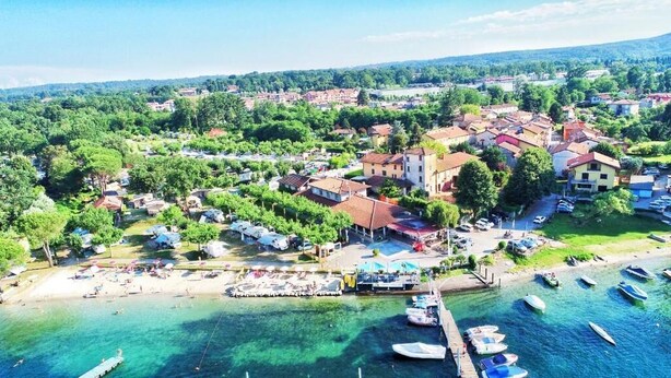 Vista aerea di una località costiera con un porto turistico, spiaggia e edifici residenziali.