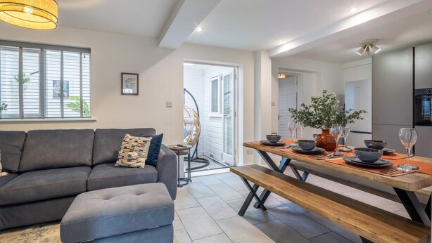 Ein modernes Wohnzimmer mit einer Couch, einem Esstisch für vier Personen und einem großen Fenster mit Jalousien.