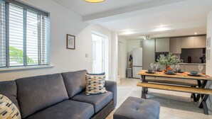 Ein modernes Wohnzimmer mit einem grauen Sofa, einem gemusterten Zierkissen und einem Holzesstisch, gedeckt mit Gläsern und einer Vase.