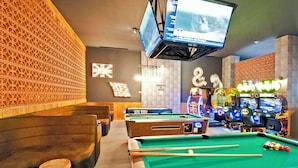 Een poolruimte met meerdere tafels, een televisie aan het plafond en achtergrondlicht van spelautomaten.
