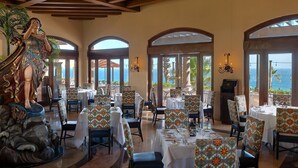 Een restaurant met tafels en stoelen, een standbeeld en grote ramen met uitzicht op de oceaan.