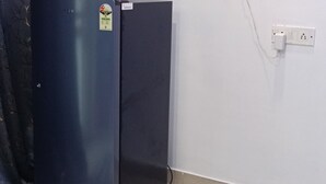 A room with a dark-colored refrigerator, a wall socket, and a power outlet.