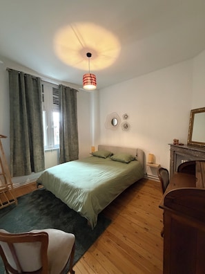 Une chambre à coucher comprenant un lit, un bureau, une chaise, une fenêtre avec des rideaux et un luminaire suspendu.