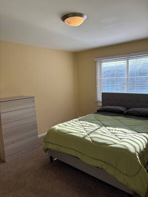 A bedroom with a bed, a dresser, and a window with blinds.