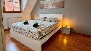 A bedroom with a bed, a radiator, a window, and a nightstand with a lamp. - Spacious, quiet apartment in the heart of Rouffach (Rouffach)
