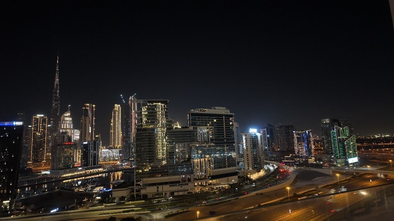 Une vue nocturne d’une ville, avec des gratte-ciel illuminés et une autoroute.