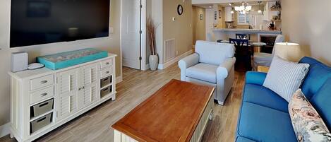 A living room with a TV, sofa, coffee table, and a dining area with chairs and a table.
