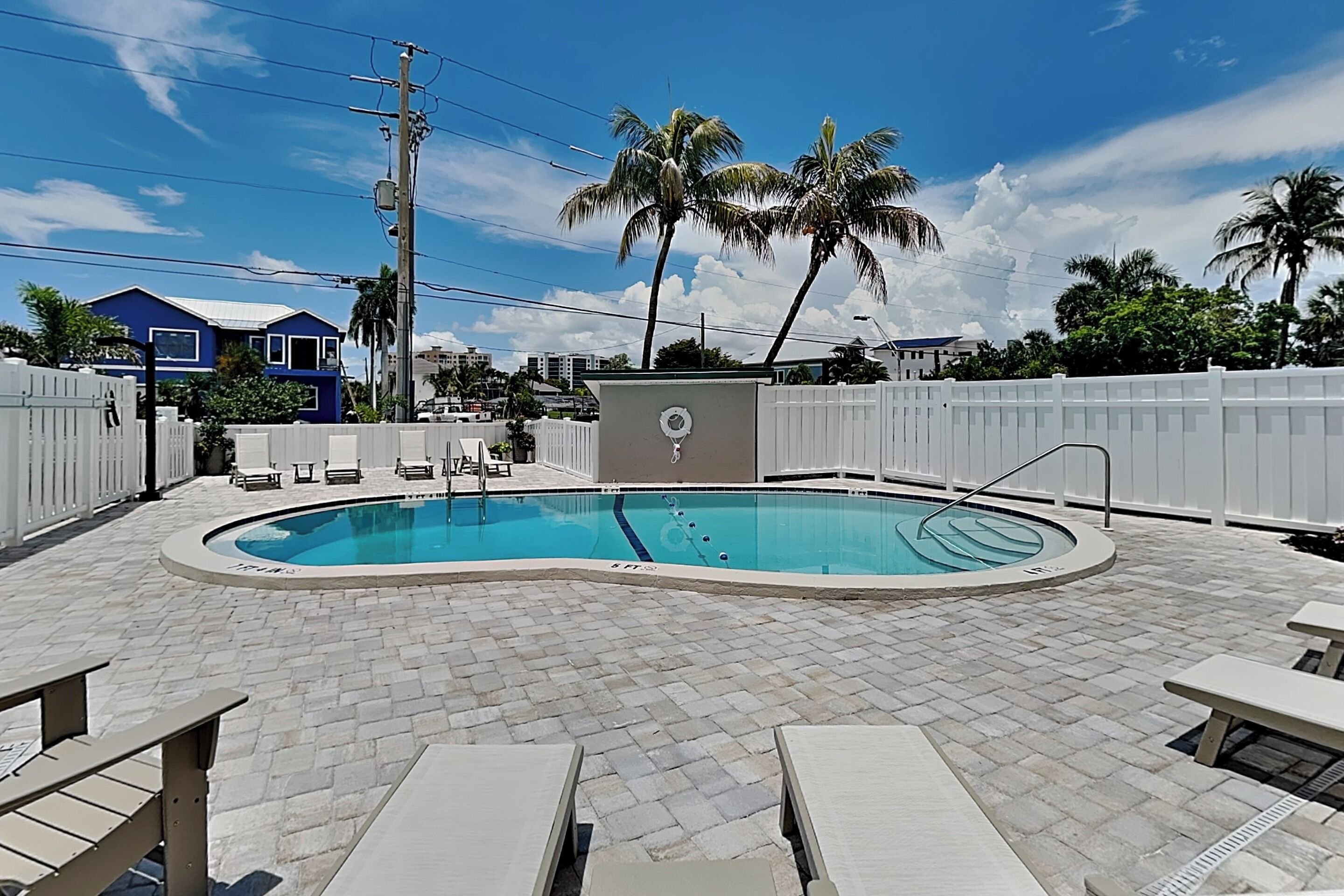 A swimming pool with lounge chairs, a small pool cover, and palm trees in the background.