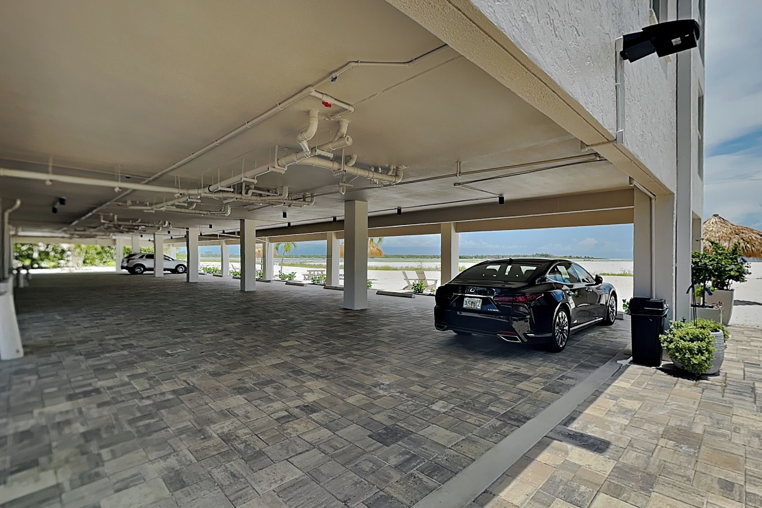 A covered parking area with a car, a view of the sea, and a building with a white exterior.