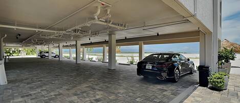 A covered parking area with a car, a view of the sea, and a building with a white exterior.