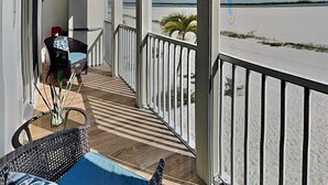 A balcony with a view of the beach, a wicker chair, a table, and a railing. - Castle Beach 105 (Fort Myers Beach)