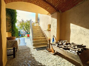 Una escalera de piedra que sube a un nivel superior, un banco de madera rústica, una cesta de mimbre y una pila de leña.