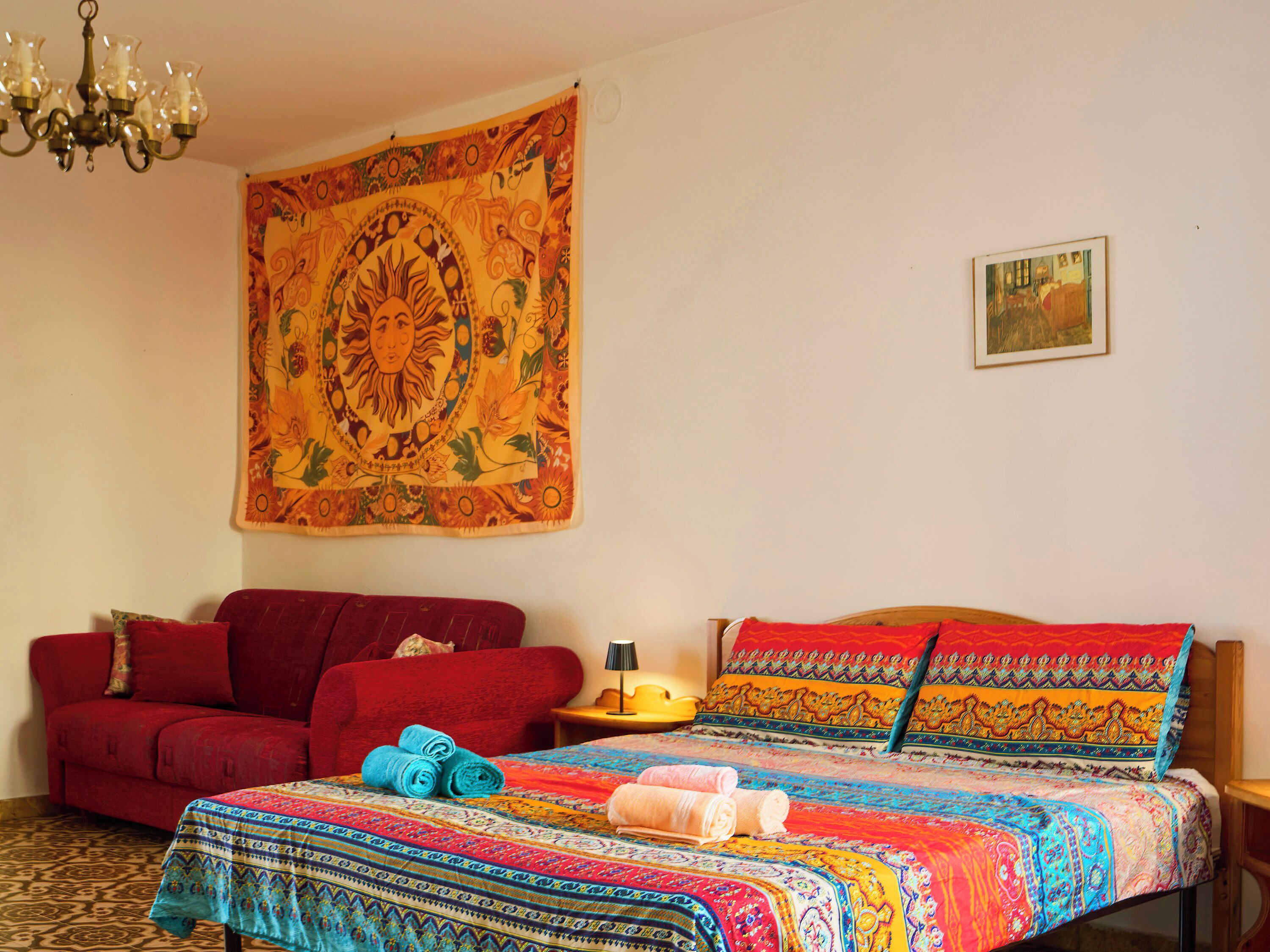 Ein Zimmer mit einem gemusterten Bettbezug, einem roten Sofa und einem Wandteppich.