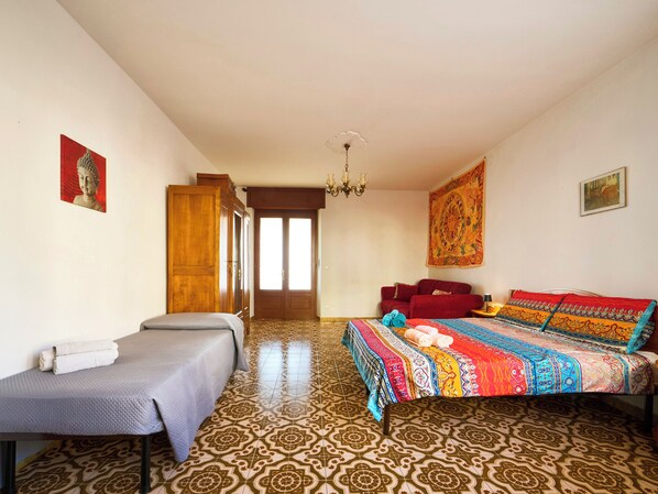 Una habitación con una cama, un sofá, un armario de madera, un tapiz y un suelo estampado.