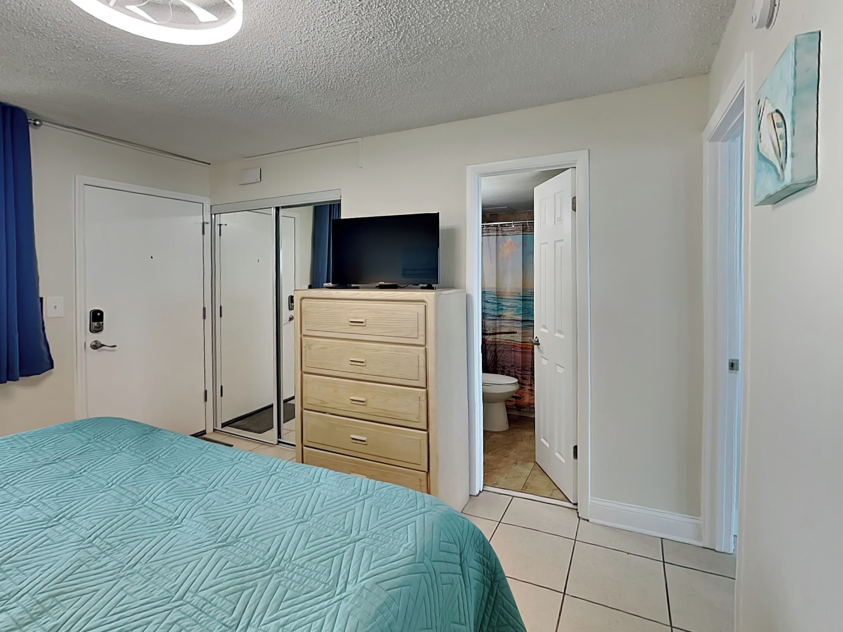 Een slaapkamer met een bed, een dressoir, een televisie en een badkamer, zichtbaar door een open deur.
