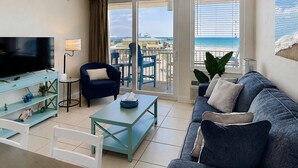 Un salon équipé d’un téléviseur, d’un canapé, d’une table basse et d’un balcon offrant une vue sur la plage.