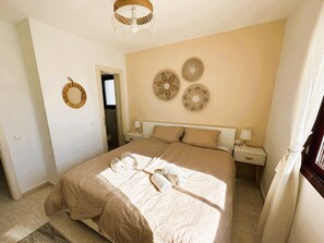 A bedroom with a large bed, two bedside tables, a hanging light fixture, and decorative wall art.